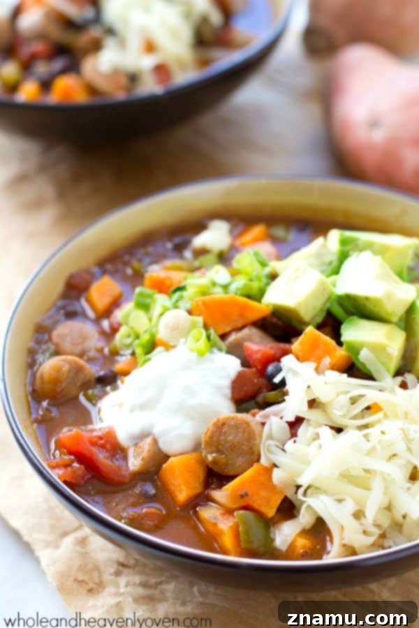 Hearty Slow Cooker Sweet Potato Sausage Chili 7 A vibrant bowl of Sweet Potato Sausage Chili topped generously with fresh, colorful garnishes.