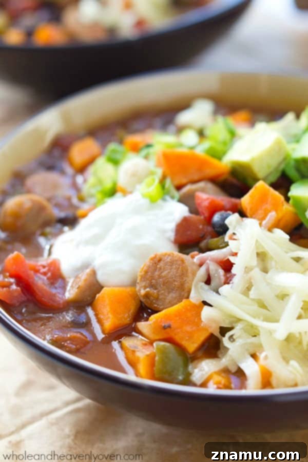 Hearty Slow Cooker Sweet Potato Sausage Chili 8 A wide shot of a crockpot full of steaming Sweet Potato Sausage Chili, with bowls and toppings arranged around it.