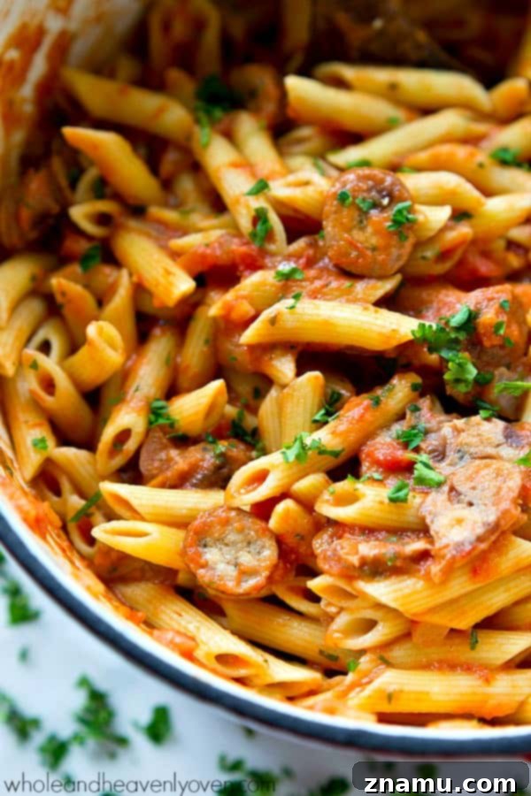 Effortless 30-Minute Penne Vodka with Sausage 3 A close-up shot of creamy penne sausage alla vodka in a dark blue dutch oven, garnished with fresh basil.