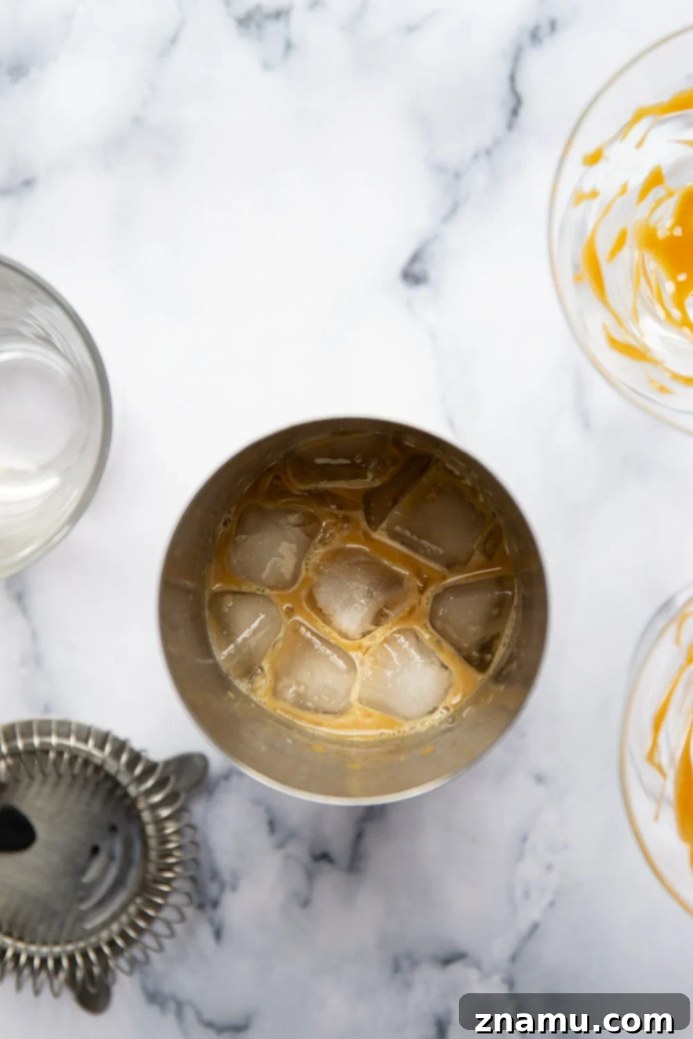 The Salted Caramel Espresso Martini 4 Ingredients for a Salted Caramel Espresso Martini laid out on a table, including bottles of vodka, coffee liqueur, espresso, and caramel syrup.