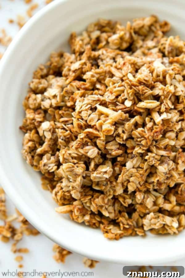 Hands breaking apart large clusters of freshly baked almond butter chai spice granola, ready for serving