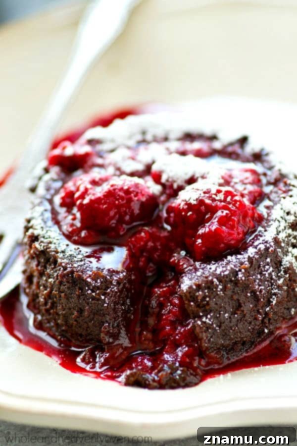 Molten Chocolate Raspberry Dream 7 Two chocolate lava cakes, one with a spoon inserted, resting on white plates and surrounded by fresh raspberries, ready for a romantic dessert.