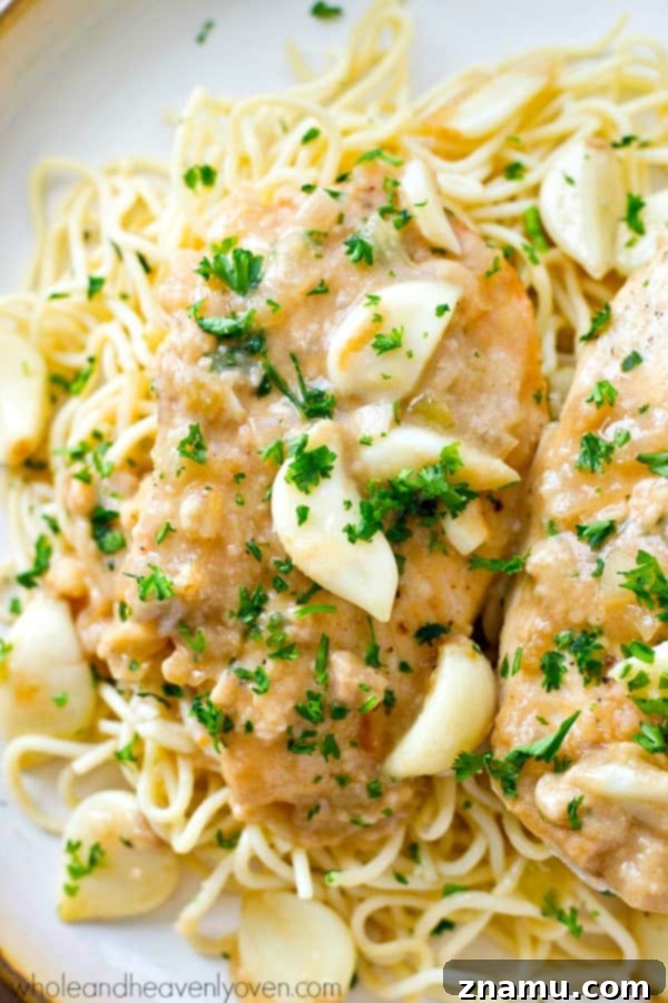 A close-up view of whole garlic cloves simmering alongside chicken breasts in a rich sauce inside a crockpot.