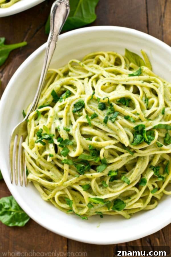 Guilt-Free Creamy Spinach Fettuccine Alfredo 5 Hands mixing fresh spinach into a creamy alfredo sauce in a saucepan, demonstrating the preparation process for the healthy pasta dish.