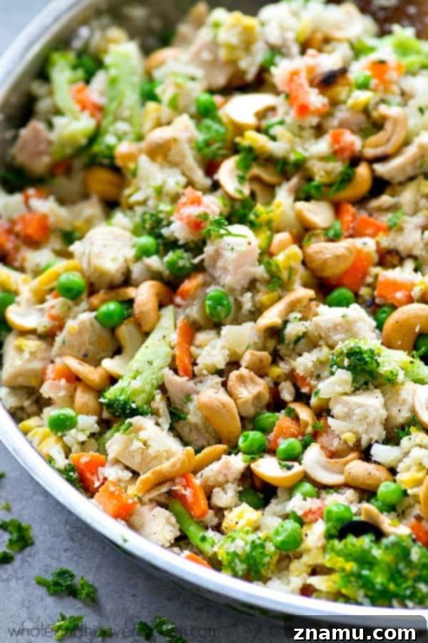 Rainbow Chicken Cauliflower Fried Rice 3 Close-up of a colorful pan of Chicken Rainbow Veggie Cauliflower Fried Rice, showcasing diced carrots, broccoli, peas, and chicken.