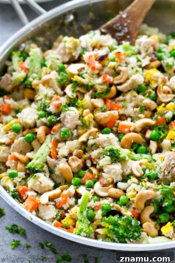 Rainbow Chicken Cauliflower Fried Rice 6 A serving spoon lifting a portion of Chicken Rainbow Veggie Cauliflower Fried Rice from a skillet, highlighting its fresh ingredients.