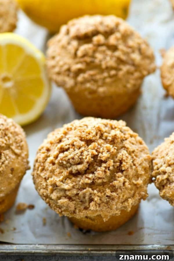 Light Lemon Streusel Greek Yogurt Muffins 3 Two freshly baked lemon crumb muffins on a rustic wooden surface, highlighting the fluffy interior and generous streusel topping.