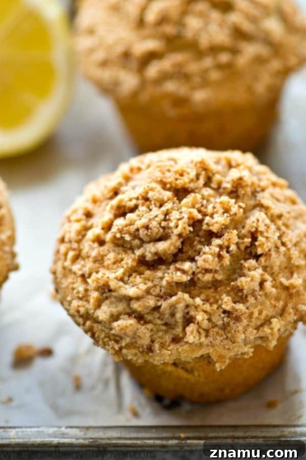 Light Lemon Streusel Greek Yogurt Muffins 4 A single lemon crumb muffin, cut in half to show its moist, light yellow interior and thick streusel layer, sitting on a cooling rack.