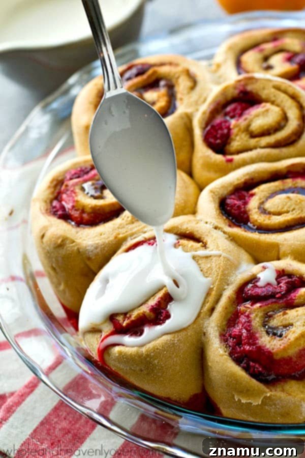 Zesty Orange Raspberry Swirl Buns 5 Hands reaching for a warm Orange Raspberry Swirl Cinnamon Roll, highlighting its soft texture.