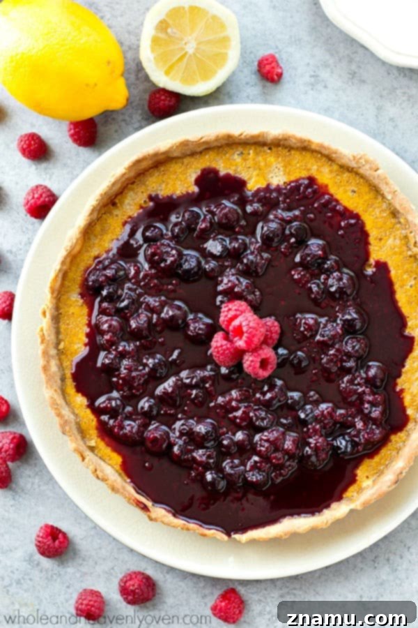 Overhead shot of a full lemon tart, glistening with berry sauce.