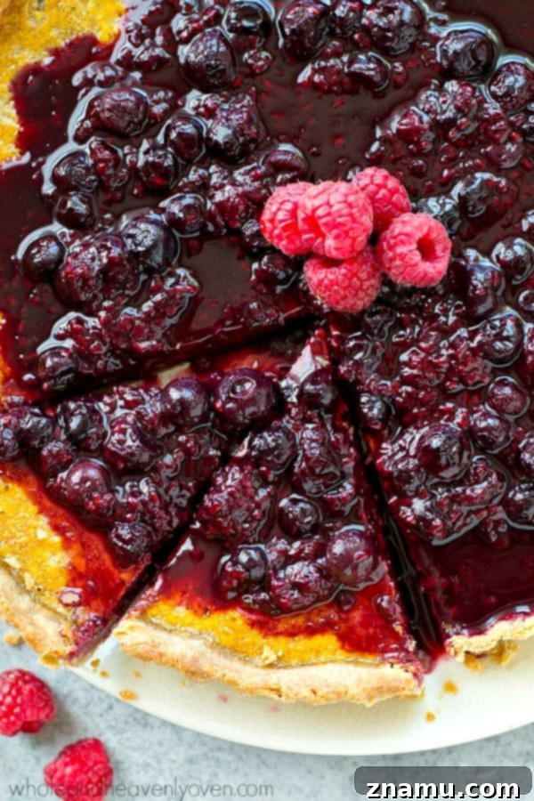 A close-up shot revealing the distinct layers of the lemon tart: crust, filling, and berry sauce.