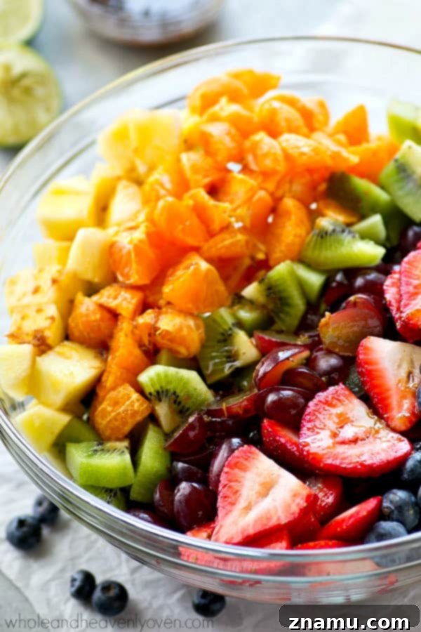 Vibrant Fruit Medley with Zesty Ginger-Lime Drizzle 2 A vibrant rainbow fruit salad with kiwi, grapes, oranges, strawberries, blueberries, and pineapple, dressed with a zesty ginger-lime dressing, photographed from above in a large white bowl.