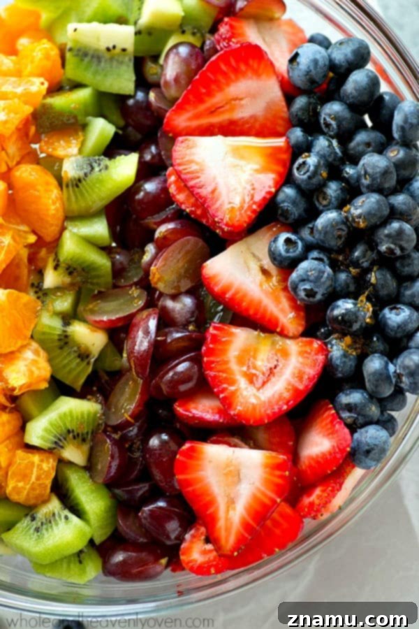 Vibrant Fruit Medley with Zesty Ginger-Lime Drizzle 3 Close-up of the rainbow fruit salad featuring sliced kiwis, halved red grapes, orange segments, strawberries, and blueberries, glistening with the ginger-lime dressing.