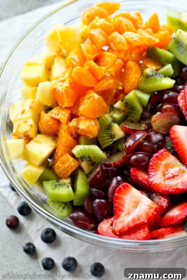 Vibrant Fruit Medley with Zesty Ginger-Lime Drizzle 4 A freshly prepared rainbow fruit salad in a glass serving bowl, highlighting the layers of colorful fruits like pineapple, oranges, grapes, and strawberries, ready for dressing.