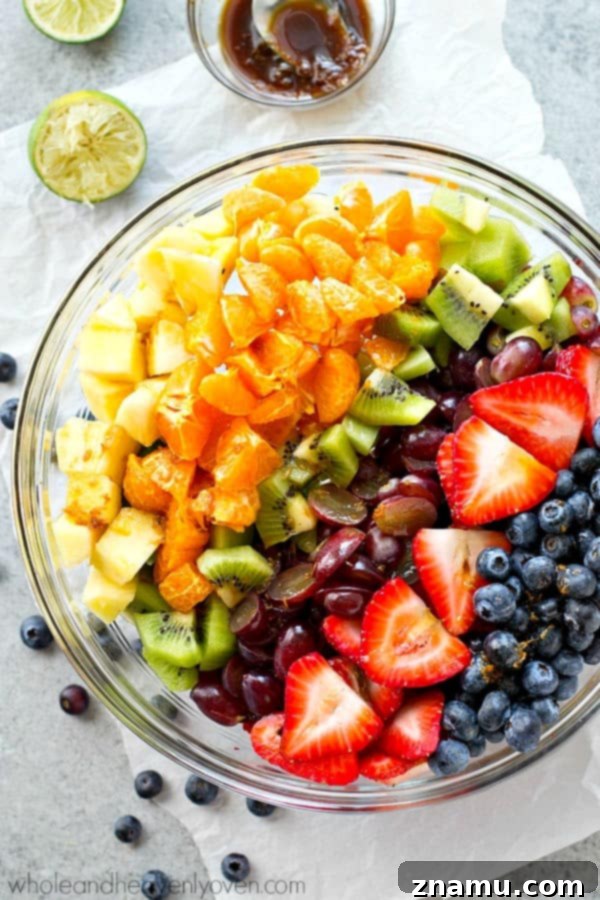 Vibrant Fruit Medley with Zesty Ginger-Lime Drizzle 5 The rainbow fruit salad mixture in a large white bowl, featuring chunks of pineapple, vibrant red strawberries, green kiwi, purple grapes, and blue blueberries, before being tossed with dressing.