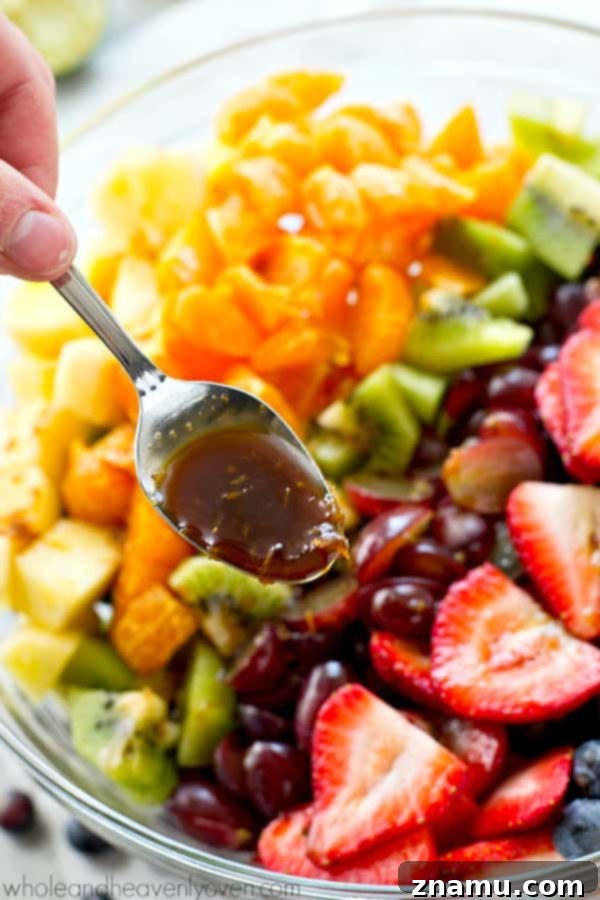 Vibrant Fruit Medley with Zesty Ginger-Lime Drizzle 6 A spoon scooping a generous portion of the rainbow fruit salad, showcasing the different fruits and the glossy ginger-lime dressing.