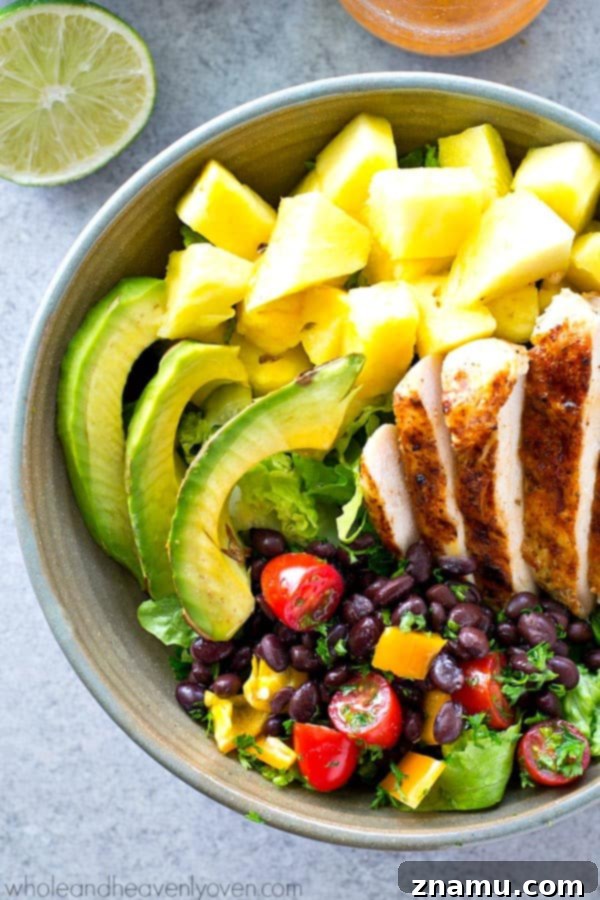 Vibrant Tropical Grilled Chicken Mexican Salad Bowls 6 A serving of Tropical Grilled Chicken Mexican Salad in a clear bowl, showing layers of green lettuce, chicken, pineapple, and other vibrant toppings, with dressing drizzled.
