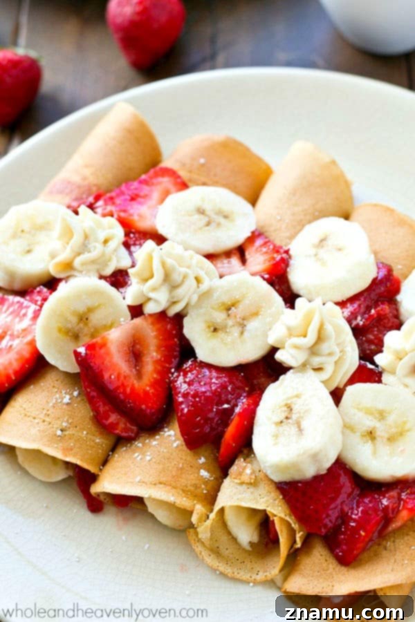Close-up of a perfectly plated Strawberry Banana Cheesecake Crepe, showcasing the vibrant fruit and creamy filling.
