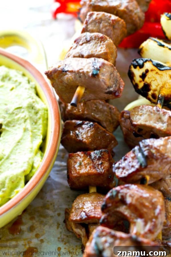 Grilled steak and pepper kebabs being dipped into a bowl of creamy avocado dip.