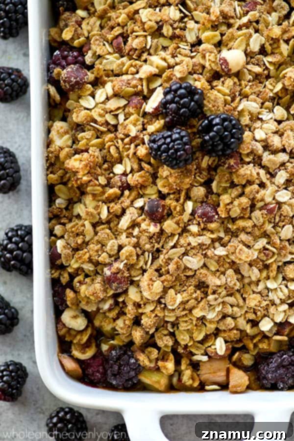 A square baking dish filled with the baked blackberry rhubarb crumble, with steam gently rising, ready to be served.