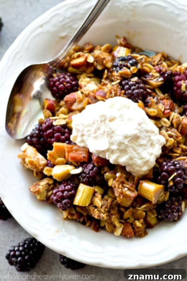 A serving of blackberry rhubarb almond crumble in a bowl, generously topped with a dollop of rich whipped cream, ready to be enjoyed.