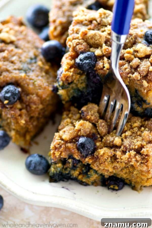 A close-up of a warm slice of blueberry banana crumb coffee cake on a plate, ready to be enjoyed.