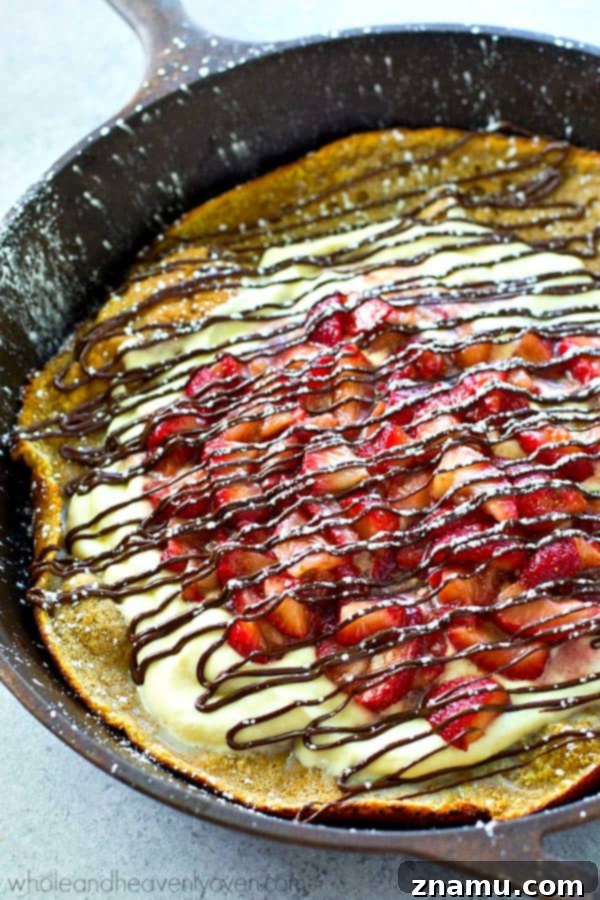 Strawberry Shortcake Oven Puff 3 A close-up view of a beautifully puffed and golden-brown Dutch Baby pancake, baked to perfection in a cast iron skillet.