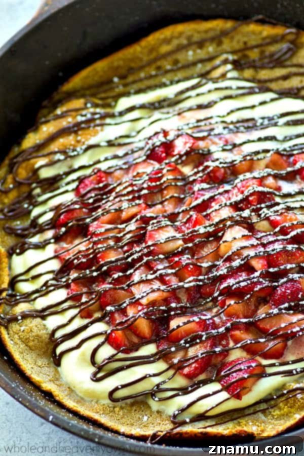 Strawberry Shortcake Oven Puff 6 An inviting overhead shot of the complete Strawberry Shortcake Dutch Baby, beautifully garnished with fresh strawberries, whipped cream, and a luscious chocolate drizzle.
