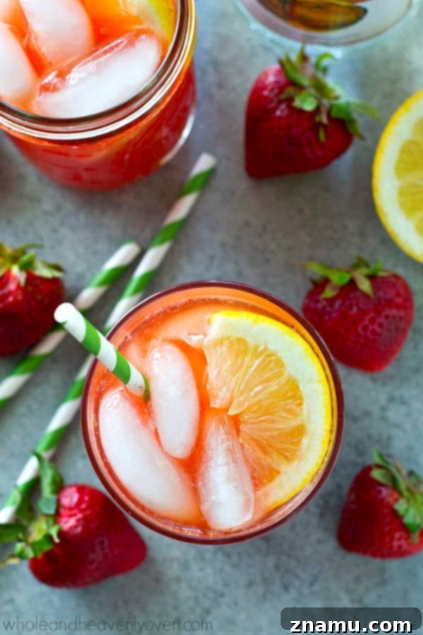 Strawberry Sunset Lemonade Cocktail 2 Refreshing Boozy Pink Strawberry Lemonade Cocktail in a glass with fresh strawberries and lemons