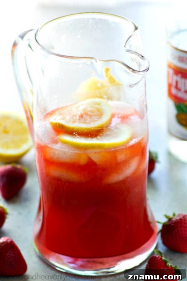 Strawberry Sunset Lemonade Cocktail 7 A hand holding a glass of the refreshing Boozy Pink Strawberry Lemonade Cocktail