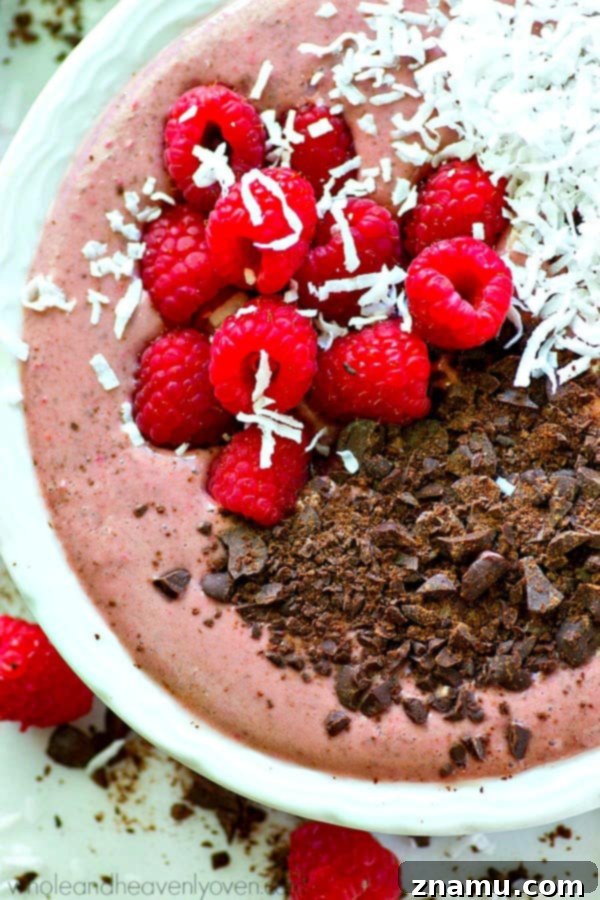 A hand holding a spoon, scooping into a colorful smoothie bowl