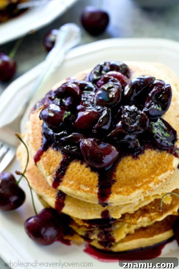Overhead shot of warm Southern-style citrus cornmeal pancakes on a plate, drenched in sweet cherry compote and garnished with fresh mint.