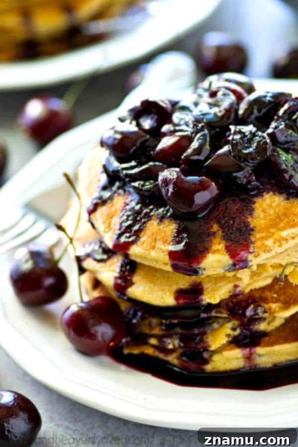 A stack of golden brown citrus cornmeal pancakes, ready to be topped, with a pitcher of milk and fresh fruit in the background.