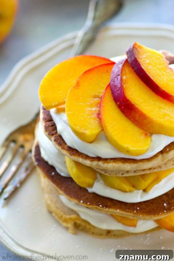 Peaches 'n' Cream Cheesecake Pancake Stacks 3 Close-up of a stacked Peaches 'n' Cream Cheesecake Pancake, highlighting the layers of golden pancake, white cream cheese filling, and thinly sliced fresh peaches.