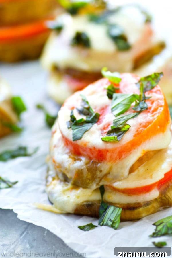 Caprese Towers with Heirloom Tomatoes and Eggplant 4 Three stacked Caprese bites on a serving plate, showing layers of succulent eggplant, colorful heirloom tomato, and melted mozzarella, topped with vibrant green basil.