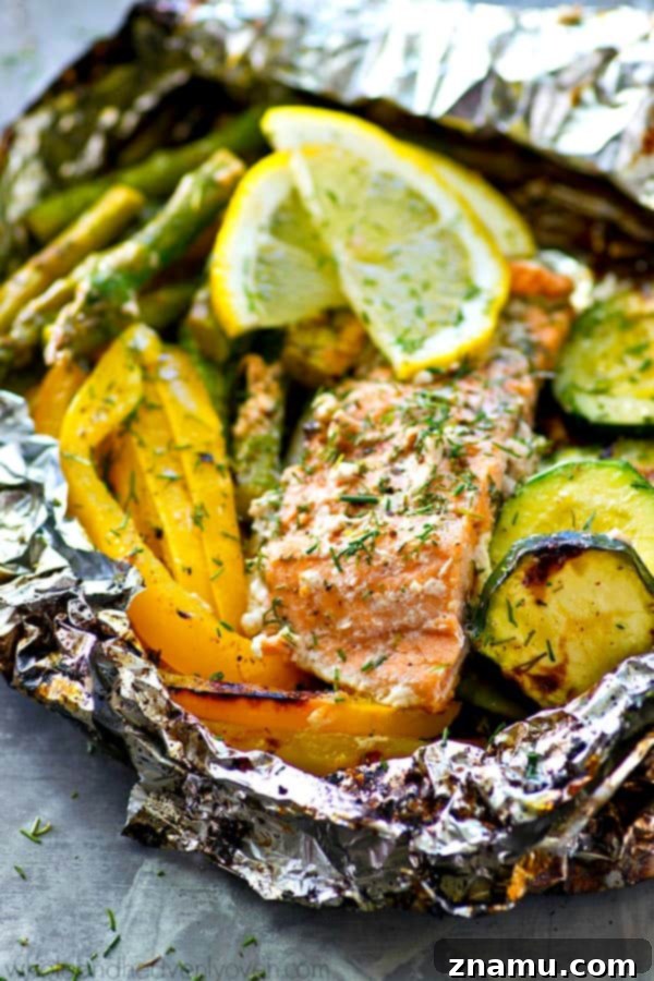 An open foil packet revealing perfectly grilled salmon, flaky and pink, alongside tender asparagus and zucchini, infused with a delicious lemon-dill marinade. Steam gently rises from the freshly cooked meal.