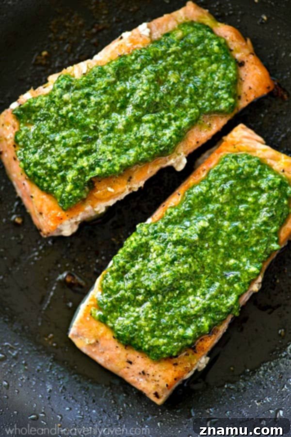 Perfectly Seared Salmon with Spinach Basil Pesto 3 Close-up of golden-brown pan-seared salmon fillets adorned with a generous dollop of green spinach basil pesto.