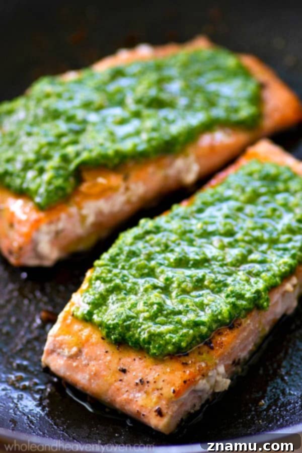 Perfectly Seared Salmon with Spinach Basil Pesto 7 A serving of pan-seared salmon heavily coated with spinach basil pesto, garnished with fresh basil leaves, ready to be enjoyed.
