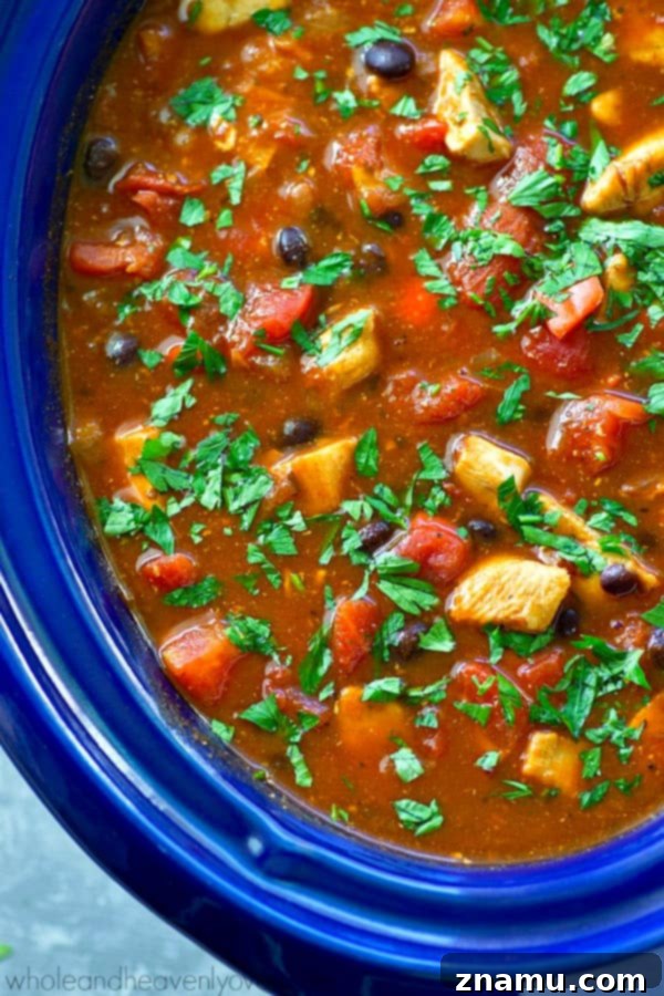 Smoky Hearty Slow Cooker Chipotle Chicken Chili 3 Close-up shot of the rich, red chipotle chicken chili simmering in a slow cooker, showcasing the chunks of chicken and beans.