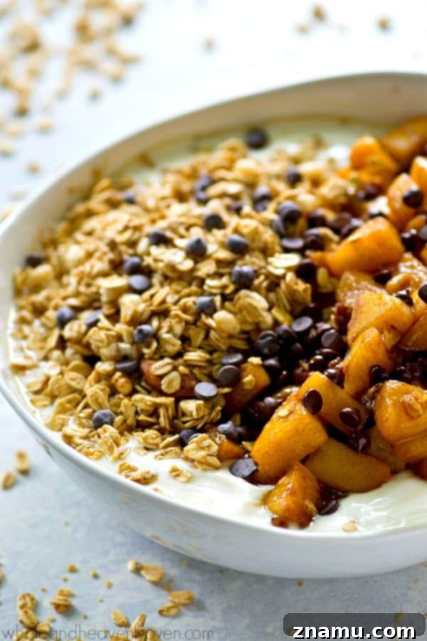 Caramel Apple Pie Flavored Granola Yogurt Bowls 6 A hand holding a spoon, scooping into a rich Caramel Apple Pie Granola Yogurt Bowl, showing the creamy yogurt and textured toppings.