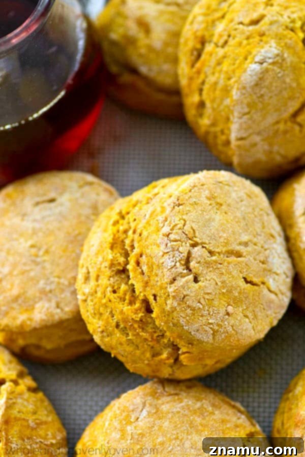 Cozy Maple Pumpkin Spice Biscuits 2 Golden brown maple pumpkin spice biscuits stacked, showcasing their flaky layers, with a drizzle of maple syrup.