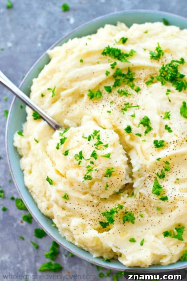 The Ultimate Creamy Garlic Whipped Potatoes 2 A close-up shot of incredibly creamy garlic whipped mashed potatoes in a white serving bowl, topped with fresh green herbs, perfect for Thanksgiving.