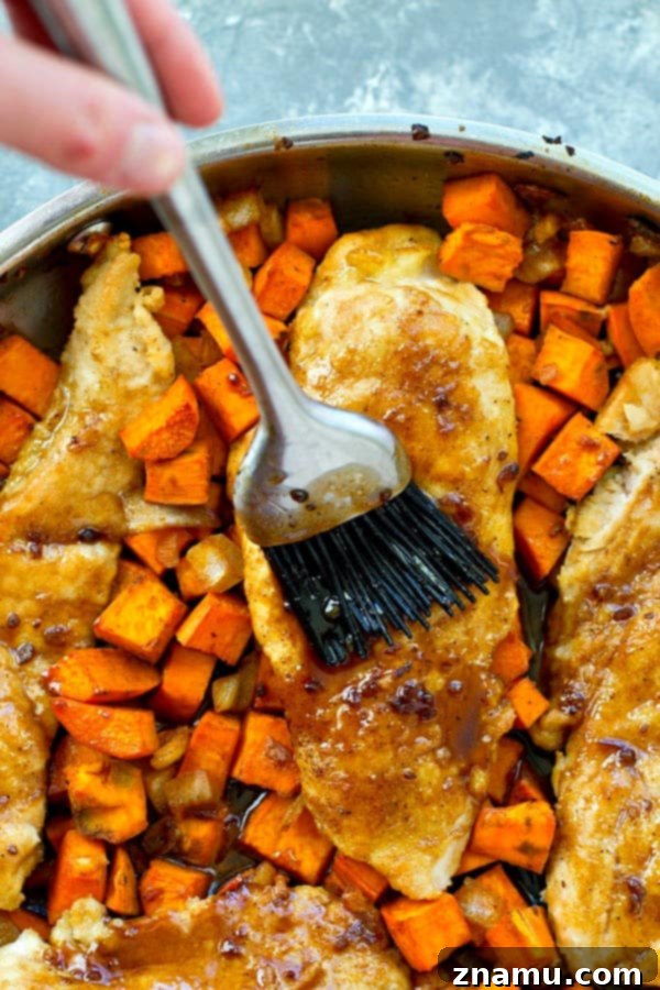Sticky Maple Chicken & Sweet Potato Hash 6 Maple syrup glaze being drizzled over cooked chicken and sweet potatoes in a skillet.