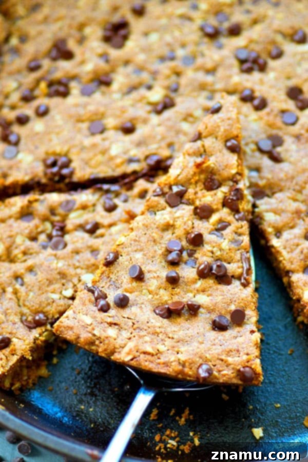 Hindistan Cevizi Yağı, Yulaf ve Damla Çikolatalı Tava Kurabiyesi 6 A fork digging into a warm, soft oatmeal chocolate chip skillet cookie, fresh from the oven, highlighting its gooey texture.
