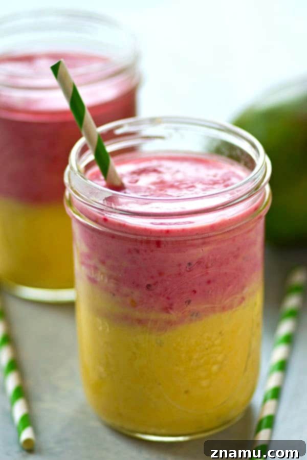 Sunrise Sunset Mango Raspberry Smoothie 3 Close-up of a two-tone mango raspberry smoothie with a straw, ready to be enjoyed.