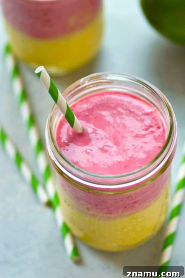 Sunrise Sunset Mango Raspberry Smoothie 4 A hand holding a glass of refreshing layered fruit smoothie, with mango and raspberry layers clearly visible.