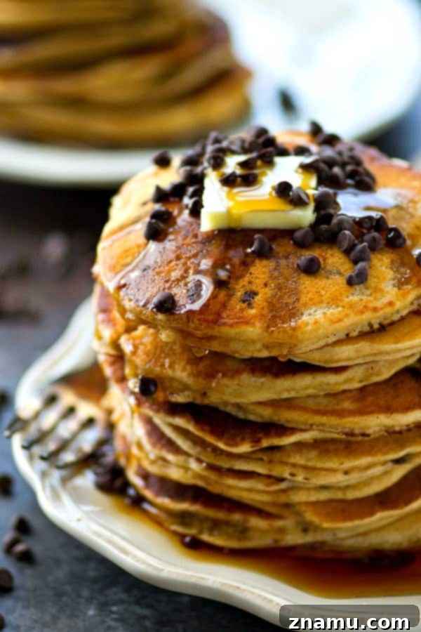 Decadent Almond Butter Chocolate Chip Flapjacks 6 A hand drizzling maple syrup over a stack of fluffy almond butter chocolate chip pancakes.