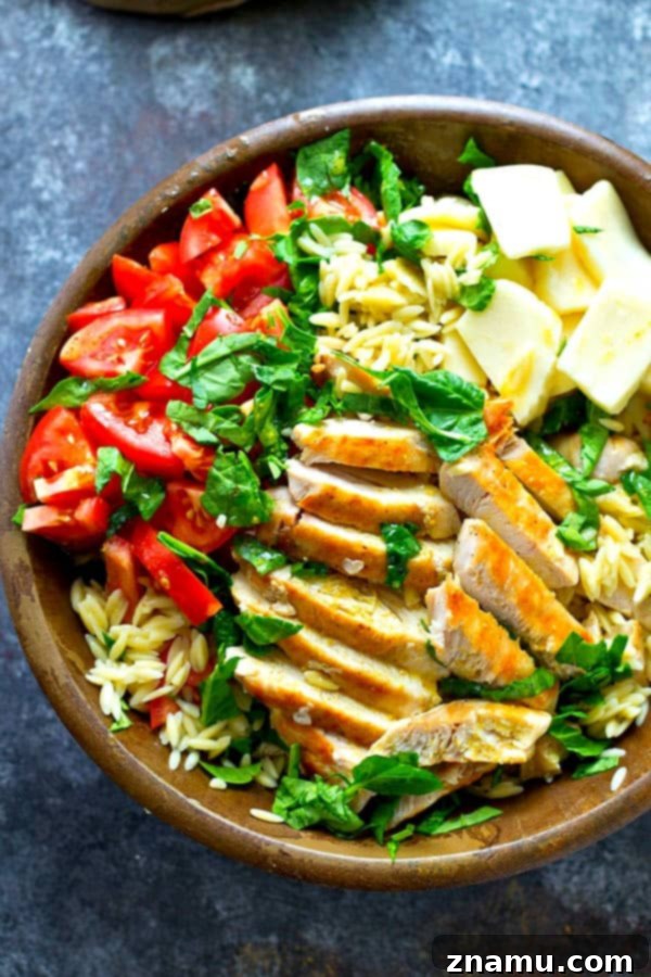 Vibrant Caprese Orzo with Grilled Chicken 5 A generous serving of Grilled Chicken Caprese Orzo Salad in a clear glass bowl, showcasing the distinct layers and colors of the ingredients. The focus is on the abundance and variety, indicating a satisfying and substantial meal that is visually appealing.