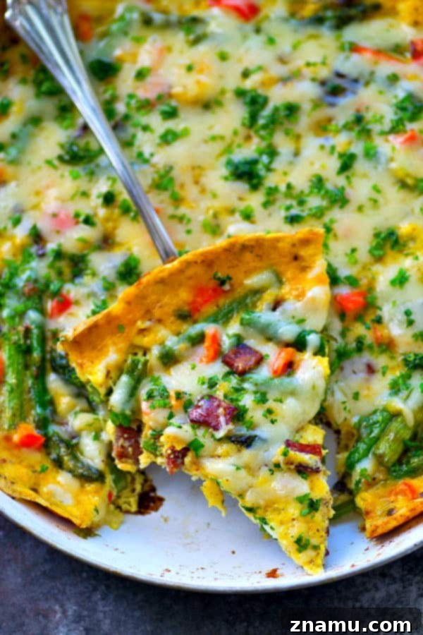Swiss Cheese, Asparagus, and Bacon Frittata 4 A slice of Swiss Cheese Asparagus Bacon Frittata on a white plate, revealing layers of fluffy egg, vibrant green asparagus, and melted Swiss cheese.