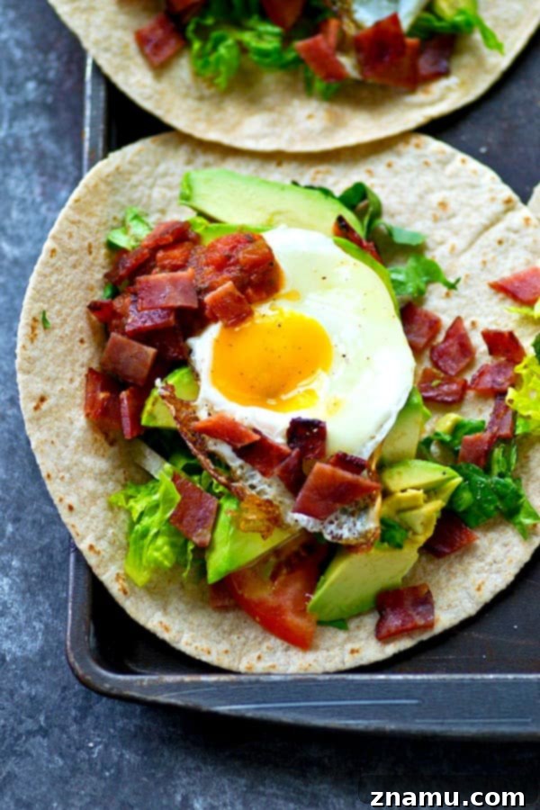 Crispy BLT Tostadas with Fried Egg and Fresh Avocado 5 A hand reaching for a BLT Fried Egg Avocado Breakfast Tostada, emphasizing its tempting, messy deliciousness.